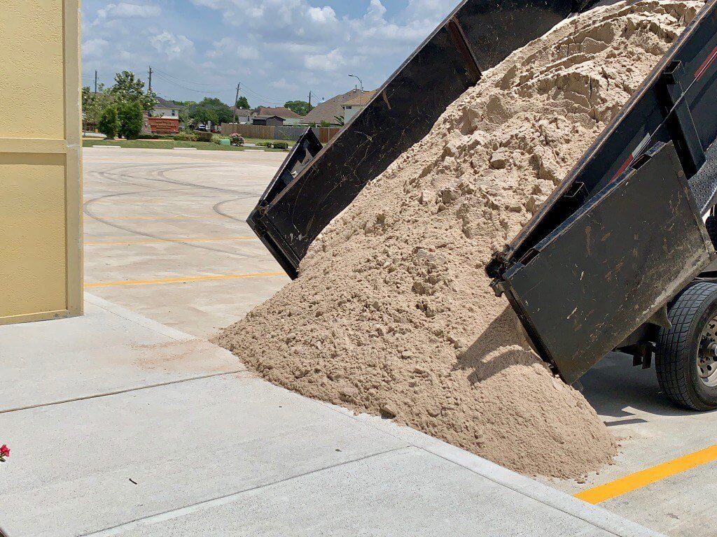 Dump trailer unloading a pile of masonry sand onto a driveway