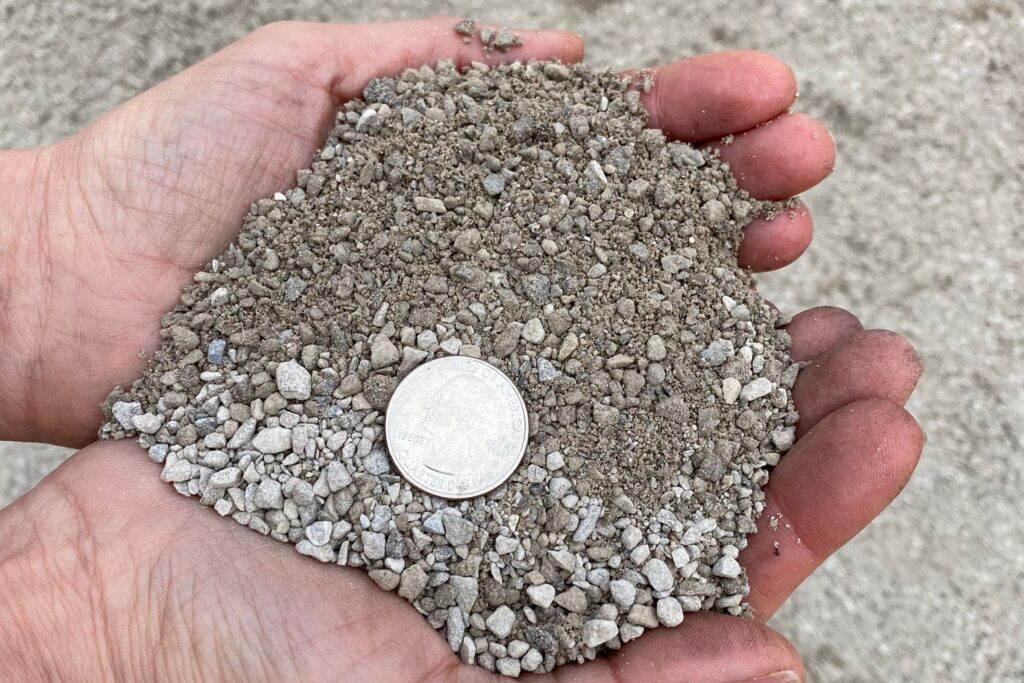 #10 Limestone Screenings — fine limestone powder and grit held in a hand with a quarter for scale